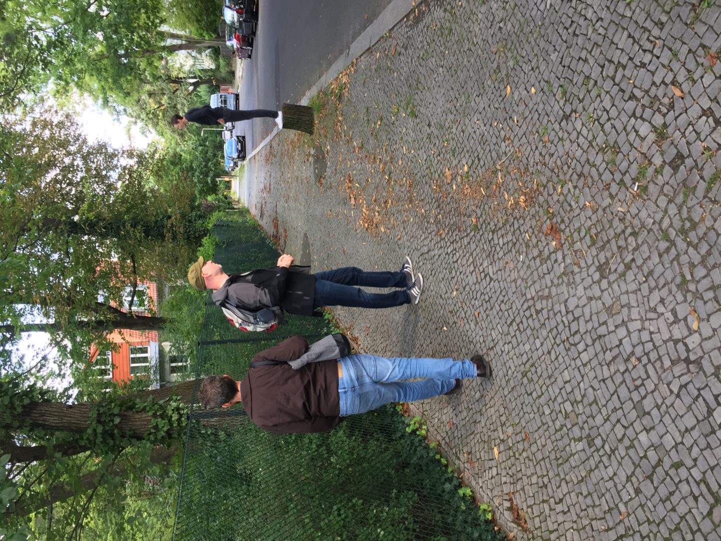 The meltwater walkers standing on a pavement trying to spot a pond on the other side of a fence. One walker is standing on a tree stump to get a better view.