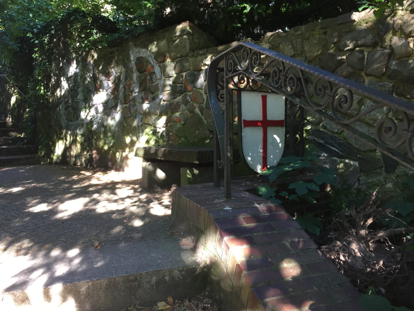 A view of some steps outside the Tempelhof Village Church. In the background is a stone wall. The handrail next to the steps is decorated with the insignia of the Knights Templar: the St. George's cross.